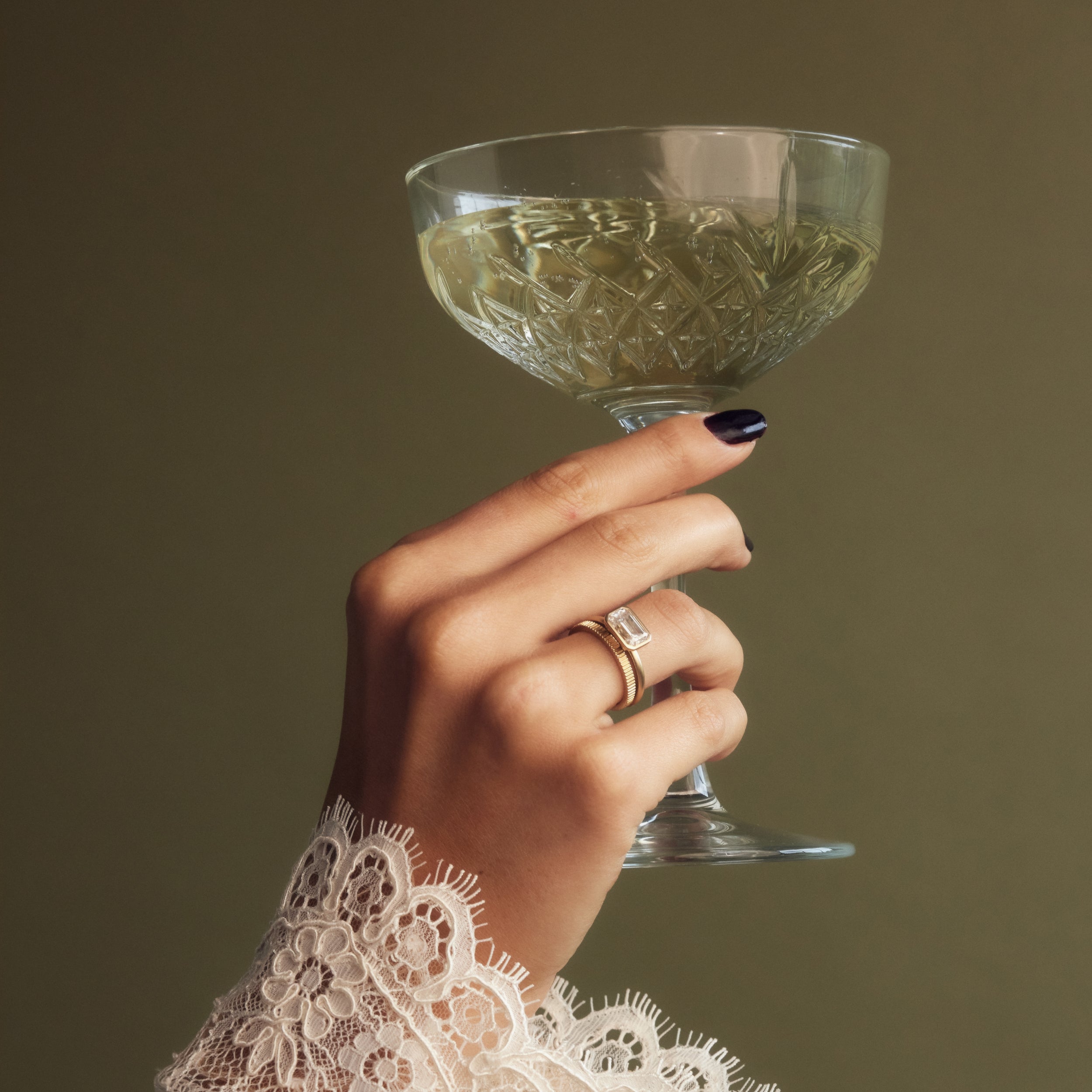 Moissanite solitaire bezel set emerald cut engagement ring on hand holding champagne glass